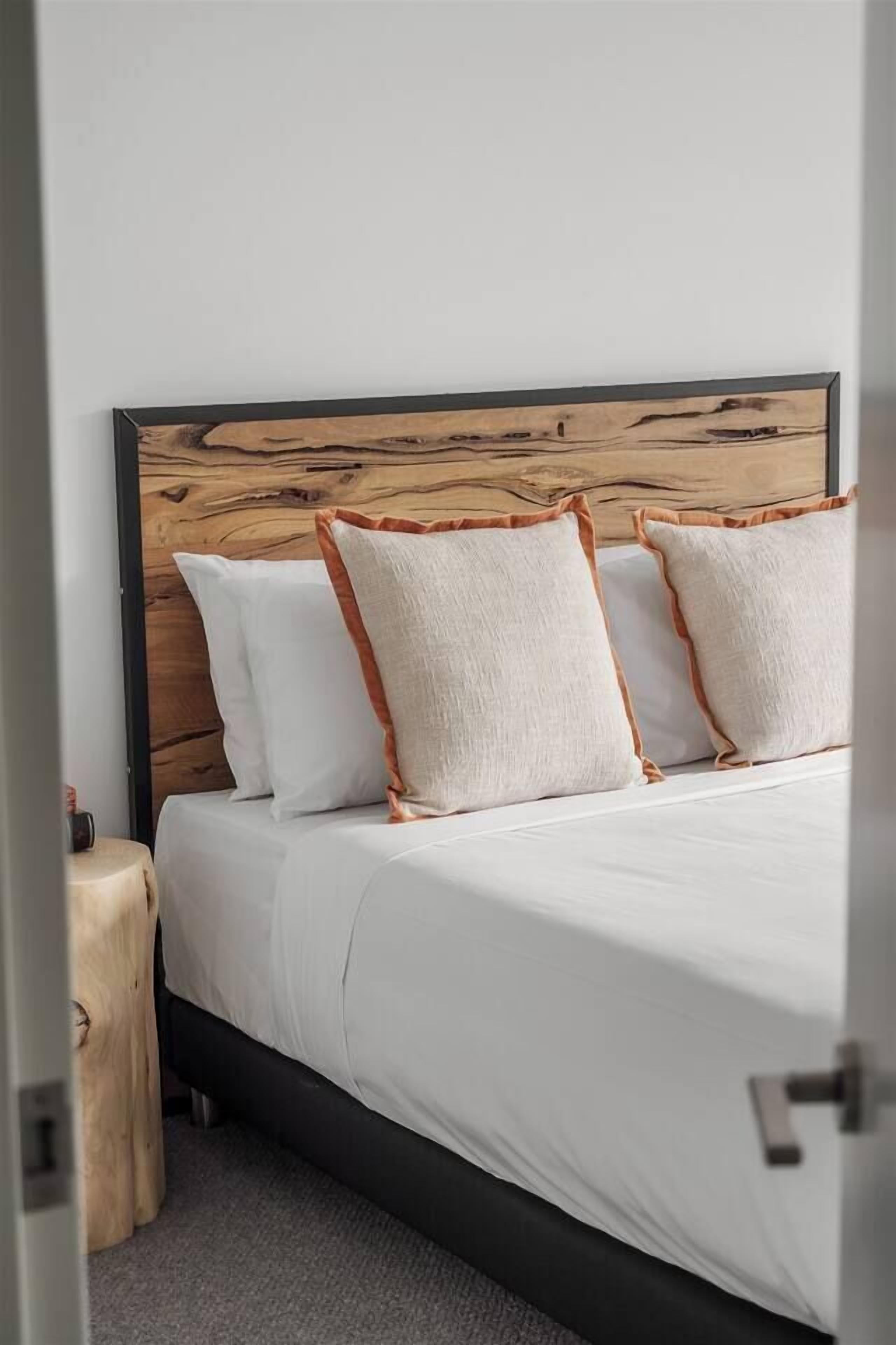 A bed with a wooden headboard, white bedding, and orange-trimmed pillows.