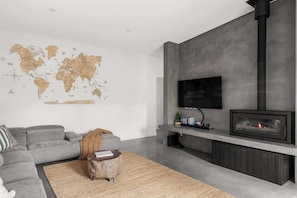 A modern living room with a grey sofa, a world map wall decoration, a flat-screen TV, and a built-in fireplace.