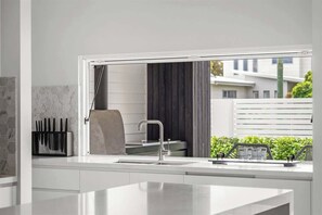 A modern kitchen with a large window, a built-in sink, and a knife block. - Burnished Bay—Coastal Luxe near Abbey Beach (Abbey)