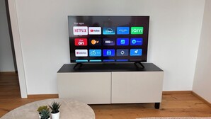 Ein Flachbildfernseher auf einem weißen Schrank, verschiedene Streaming-Apps werden angezeigt.