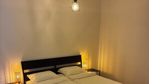 Ein ordentlich bezogenes Bett mit weißen Leinentüchern und zwei aufgerollten Handtüchern, ein dunkles Holz-Kopfteil und ein Nachttisch mit einer Lampe.