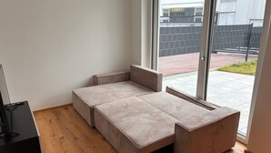 Ein modernes Zimmer mit einer Schlafsofa, einem Fernseher auf einem Beistelltisch und einem großen Fenster mit Blick ins Freie.