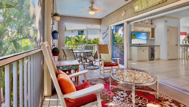 A spacious balcony with a dining area, a TV, and a kitchen visible through an open door. - Ilha Bella-Private pool in Holmes Beach (Holmes Beach)