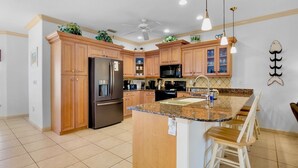 A kitchen with wooden cabinets, a granite countertop, a refrigerator, a microwave, and a ceiling fan. - Ilha Bella-Private pool in Holmes Beach (Holmes Beach)