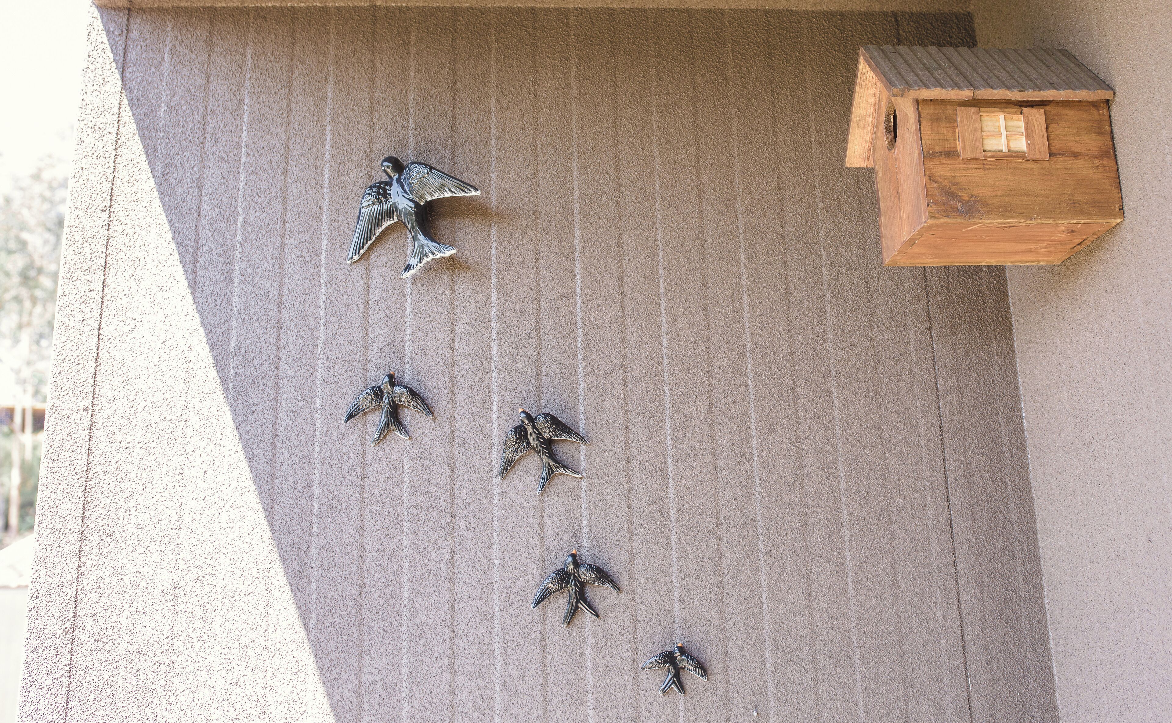 A birdhouse attached to a wall with several bird figurines arranged in a descending order.