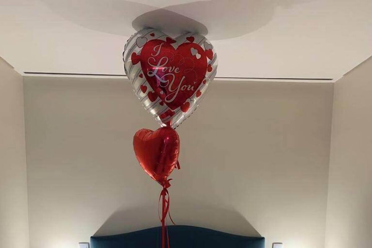 Una cama bien hecha con toallas enrolladas, un globo decorativo con forma de corazón y un peque ño ramo de flores.