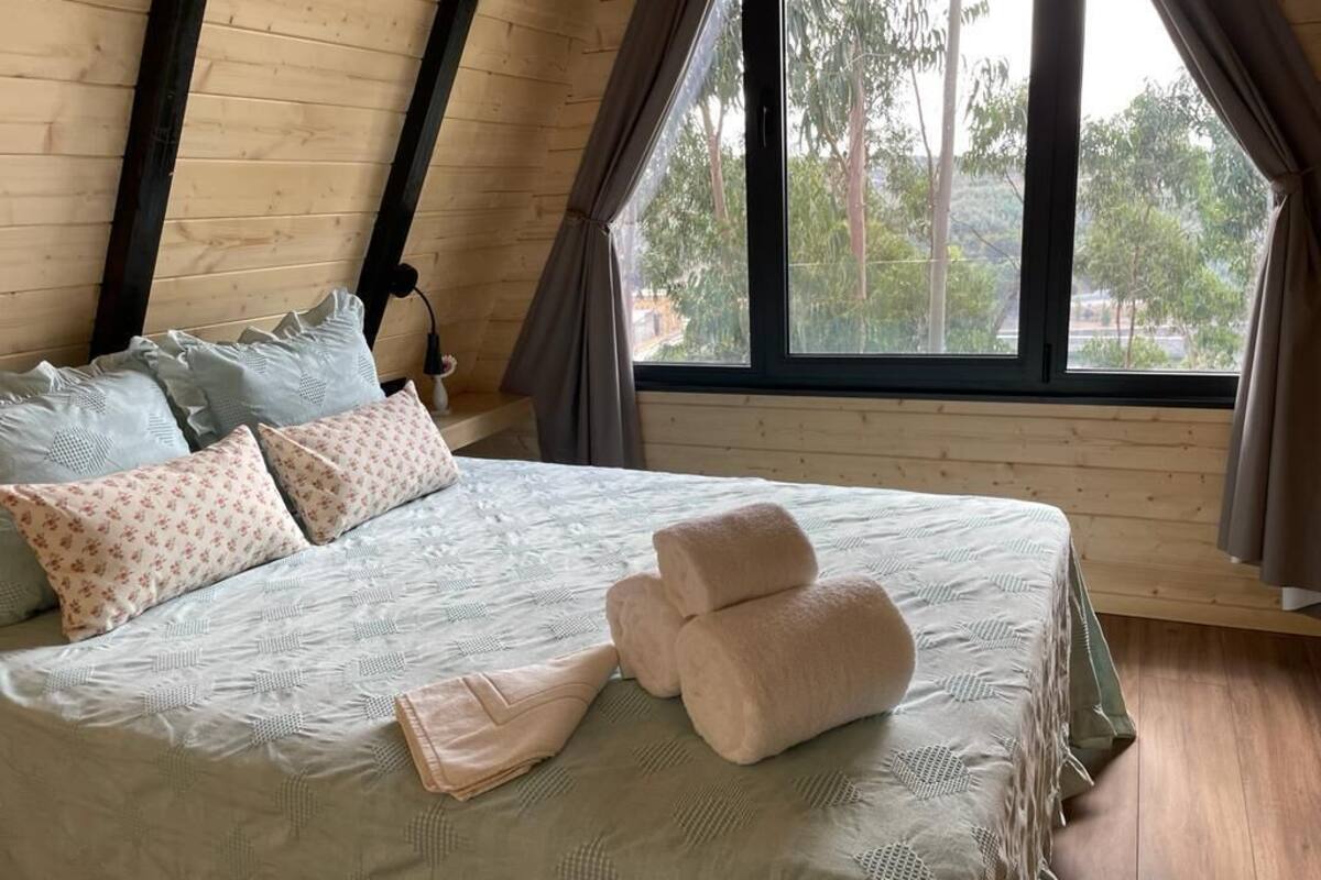 Un dormitorio con cama, almohadas y una ventana con cortinas.