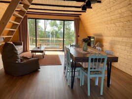 Interior acogedor de una cabaña con una mesa de madera, sillas, un sofá y una escalera.