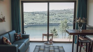 Ett vardagsrum med ett stort fönster med utsikt över en sjö och en skog, en soffa, ett soffbord och ett matbord.