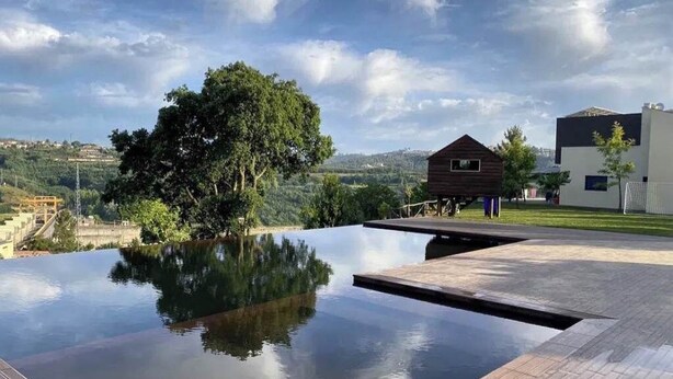 En modern infinitypool med ett trädäck, omgiven av frodig grönska och en klar himmel.