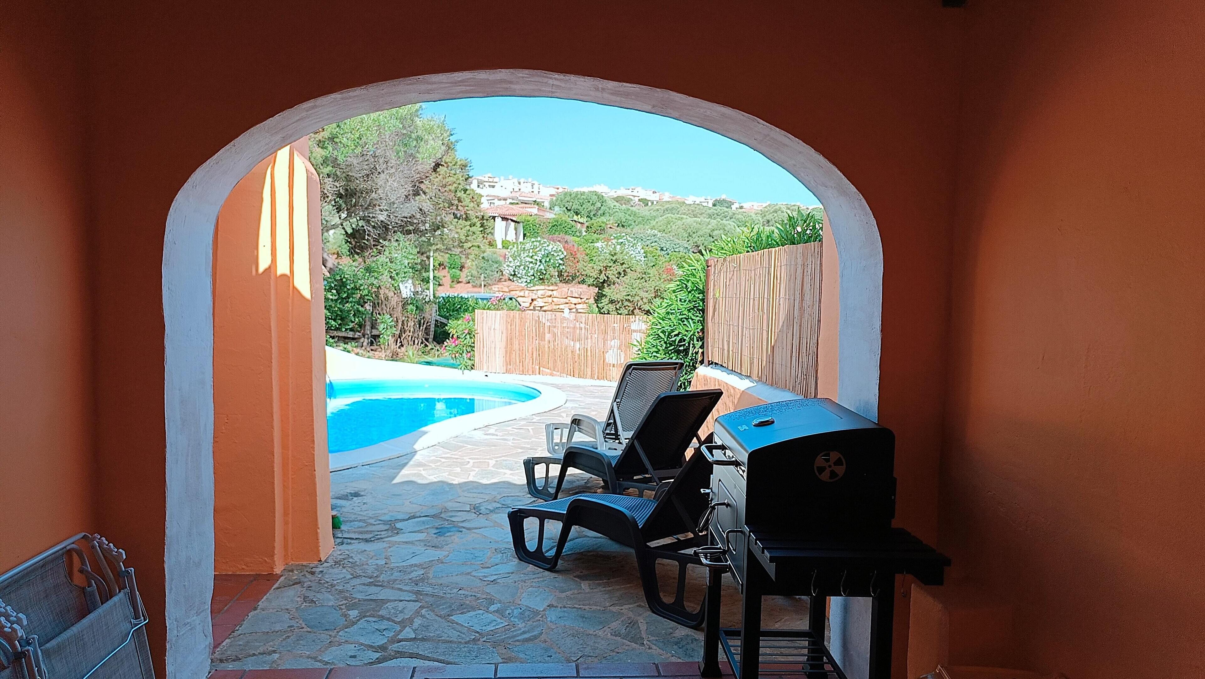 An outdoor patio with a pool, two lounge chairs, and a barbecue grill.