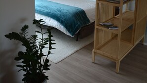 Un dormitorio con una cama, mesitas de noche, una estantería de madera con plantas, un reloj de pared y una lámpara colgante.