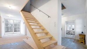 Et moderne interiør med en trappe i træ, store vinduer og et spiseområde.