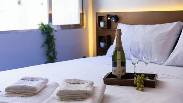 Een netjes opgemaakt bed met een fles Chandon wijn en twee glaasjes op een dienblad, samen met een tros druiven.