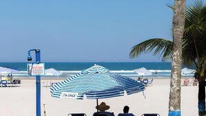 Een strand met parasols en stoelen, een bord en een palmboom.