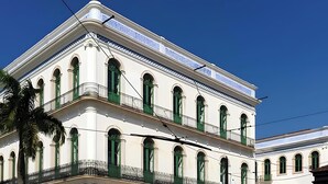 Een wit gebouw met groene raamkozijnen en balkons, met een decoratieve kroonlijst en een helderblauwe lucht op de achtergrond.