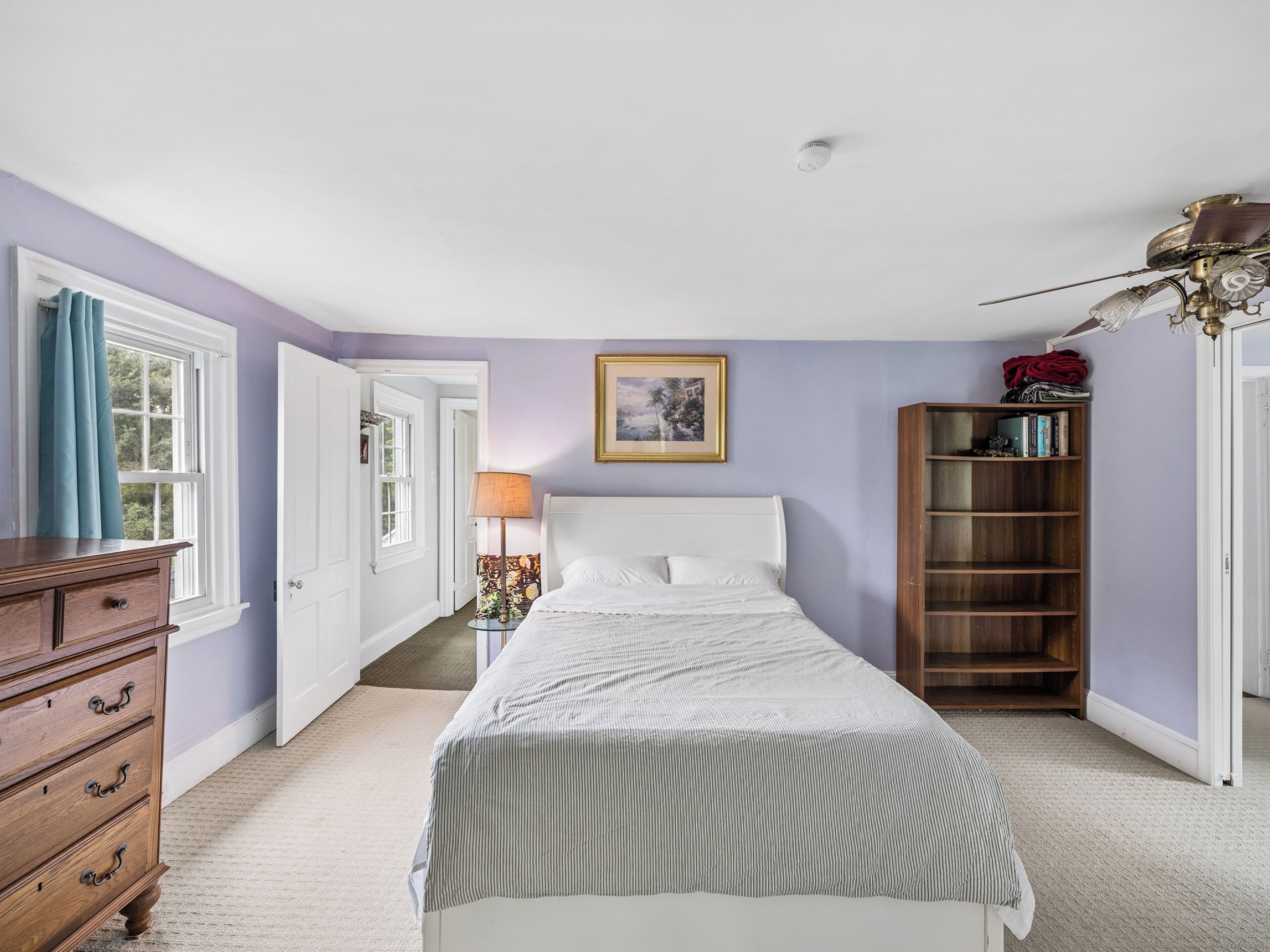 A bedroom with a bed, dresser, bookshelf, and a ceiling fan.