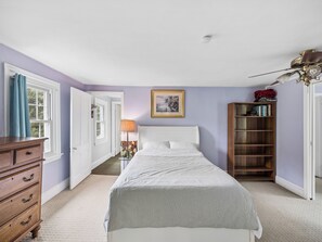 Un dormitorio con cama, cómoda, estantería y ventilador de techo.