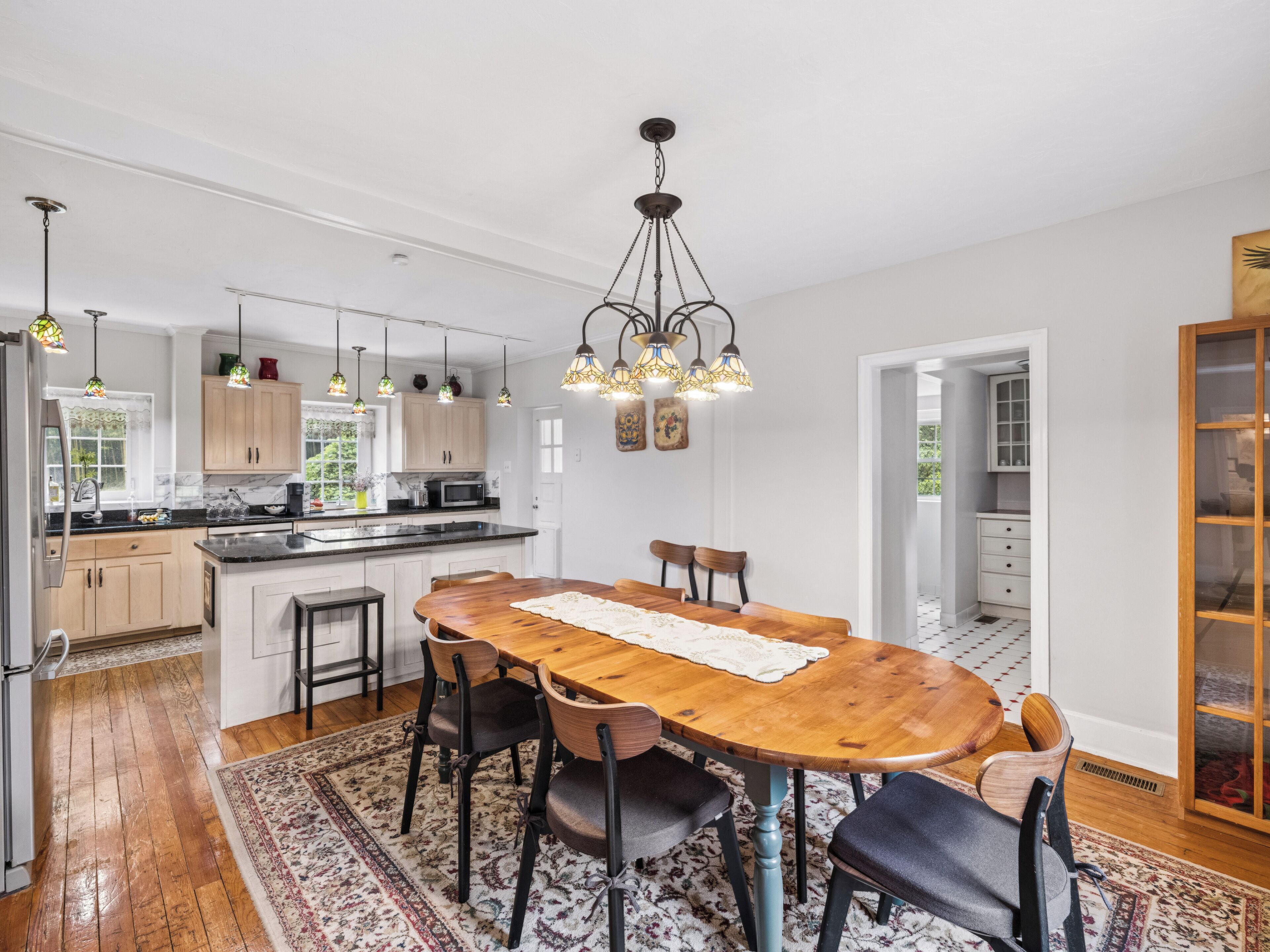 A modern kitchen with a central island, pendant lighting, and a dining area with a wooden table and chairs.