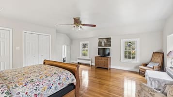 A bedroom with a bed, a dresser, a television, a chair, and a ceiling fan.