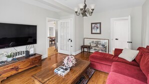 Una sala de estar con un televisor de pantalla plana, una mesa de centro de madera, un sofá rojo y una araña.