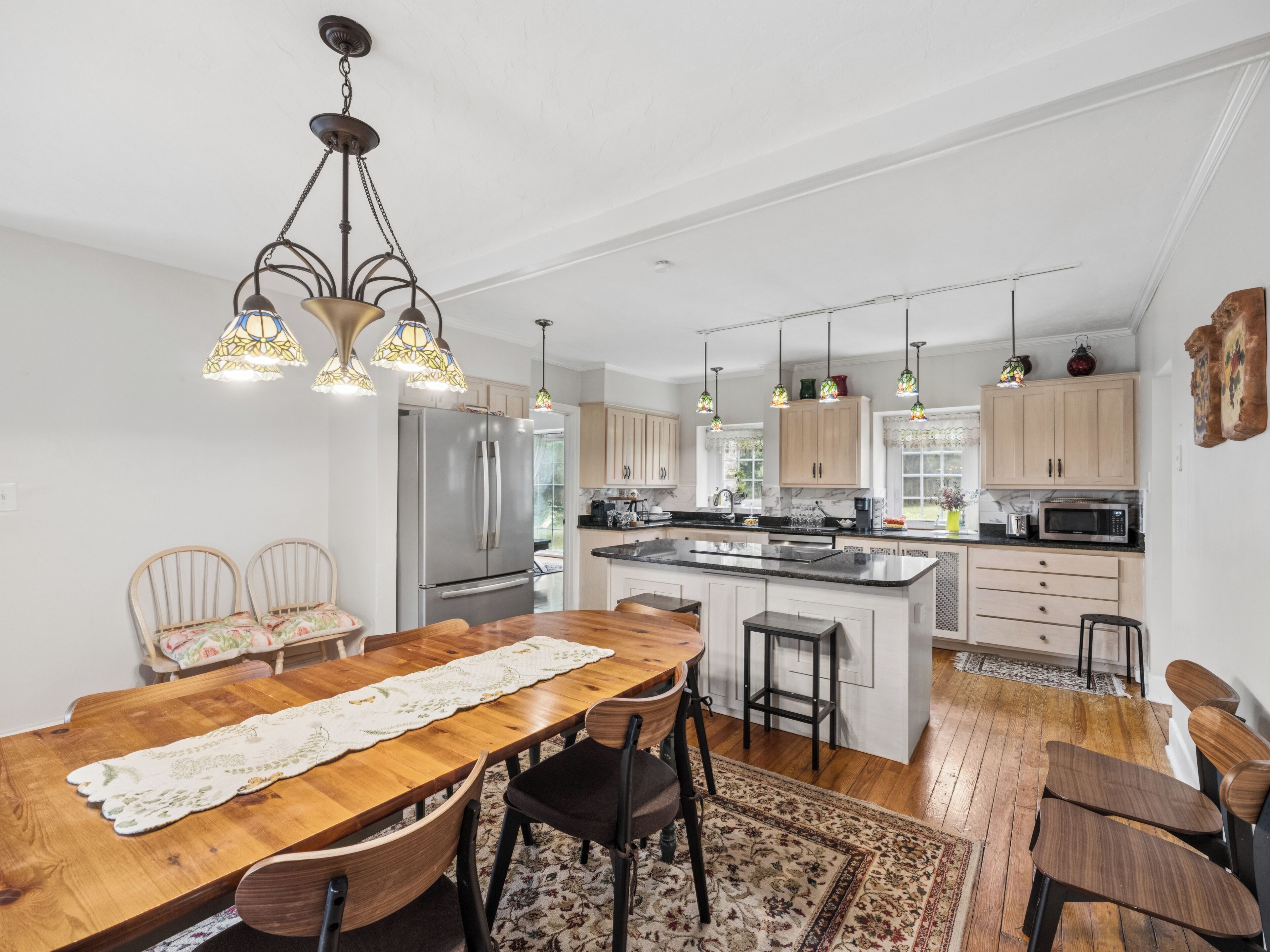 A modern kitchen with a central island, wooden dining table, and bar stools.