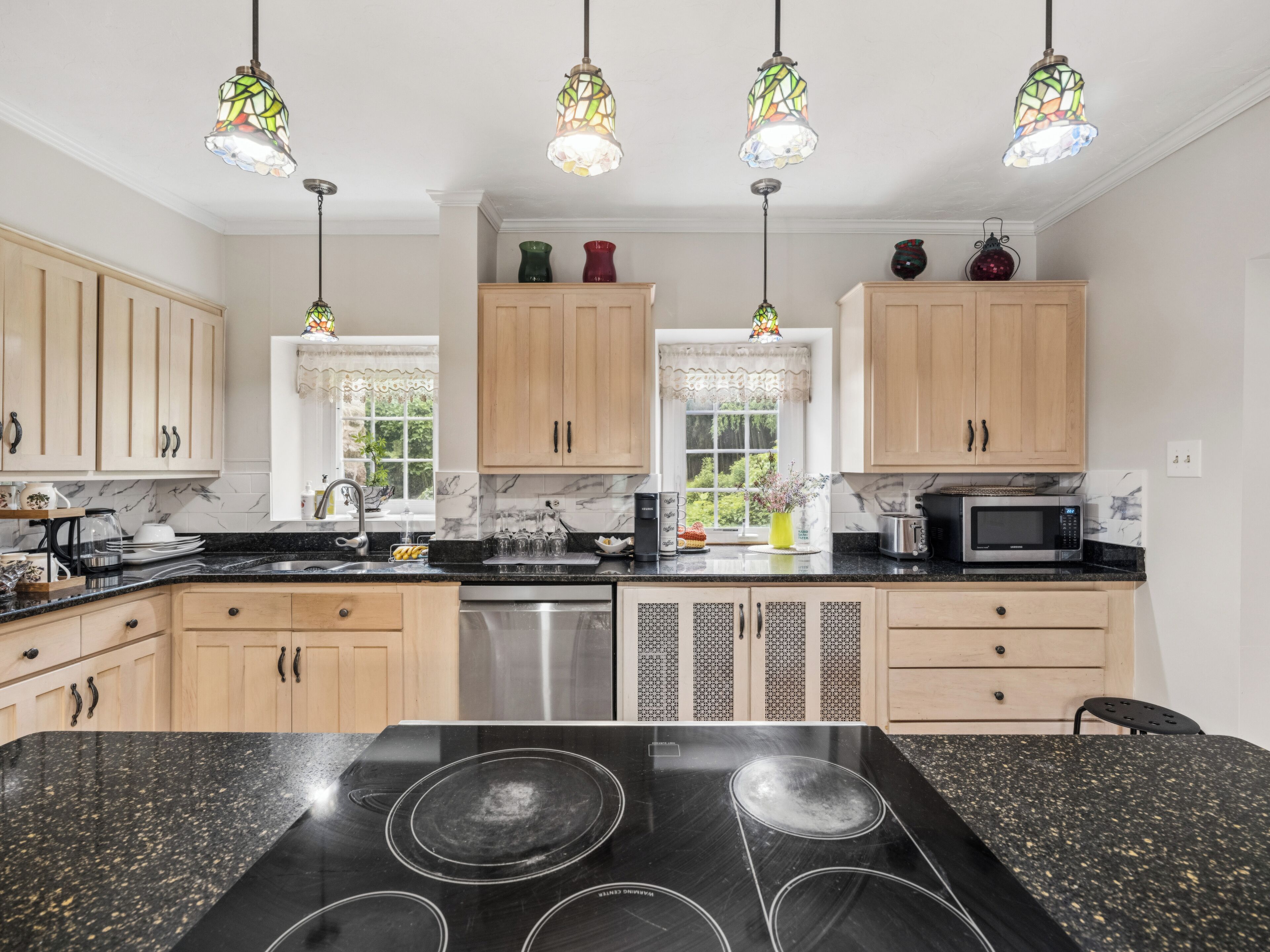 A kitchen with a black granite countertop, stainless steel appliances, wooden cabinets, and stained glass pendant lights.