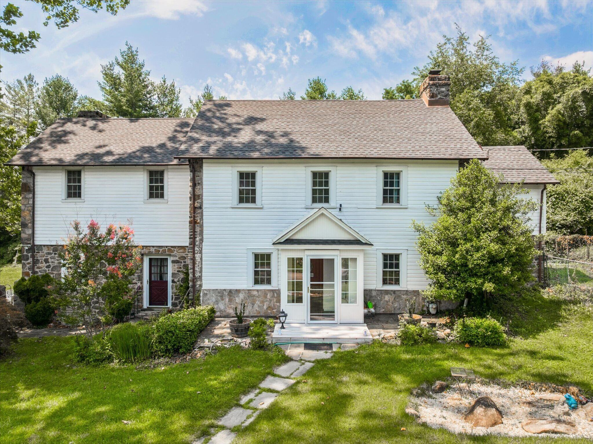 A two-story house with a stone foundation and white siding, a front porch, and a well-maintained garden.