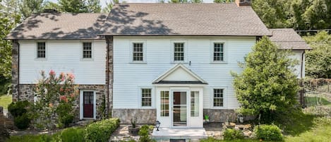 A two-story house with a stone foundation and white siding, a front porch, and a well-maintained garden.