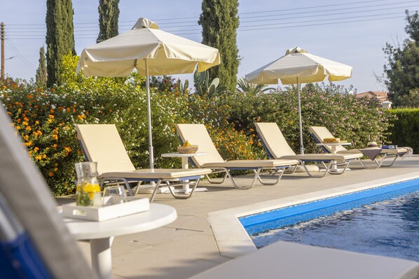 Un espace aménagé au bord de la piscine, avec des chaises longues et des parasols, entouré de verdure et de fleurs.