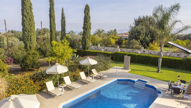 Une piscine entourée de verdure et d’un mur de pierre, avec des chaises longues et des parasols à proximité.