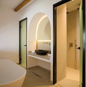A modern bathroom with a freestanding bathtub, a vanity with a bowl sink, and a shower area. - Safrani Suites (Santorini)