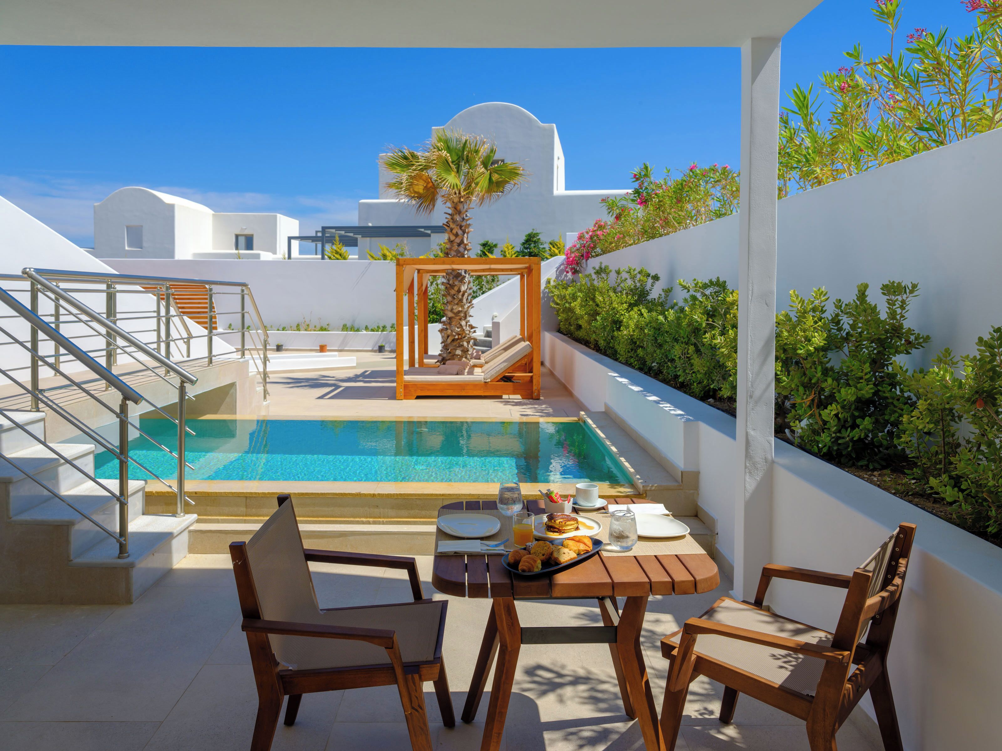 A poolside area with a table set for breakfast, chairs, and a staircase leading to an upper level.