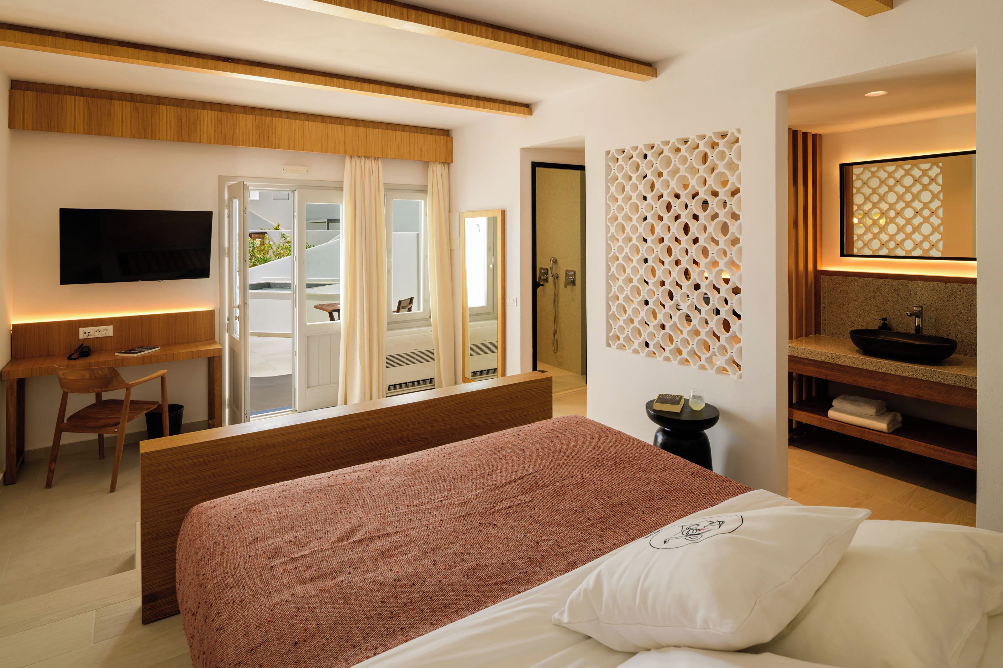 A modern hotel room with a bed, a desk, a TV, and a bathroom with a shower and toilet.