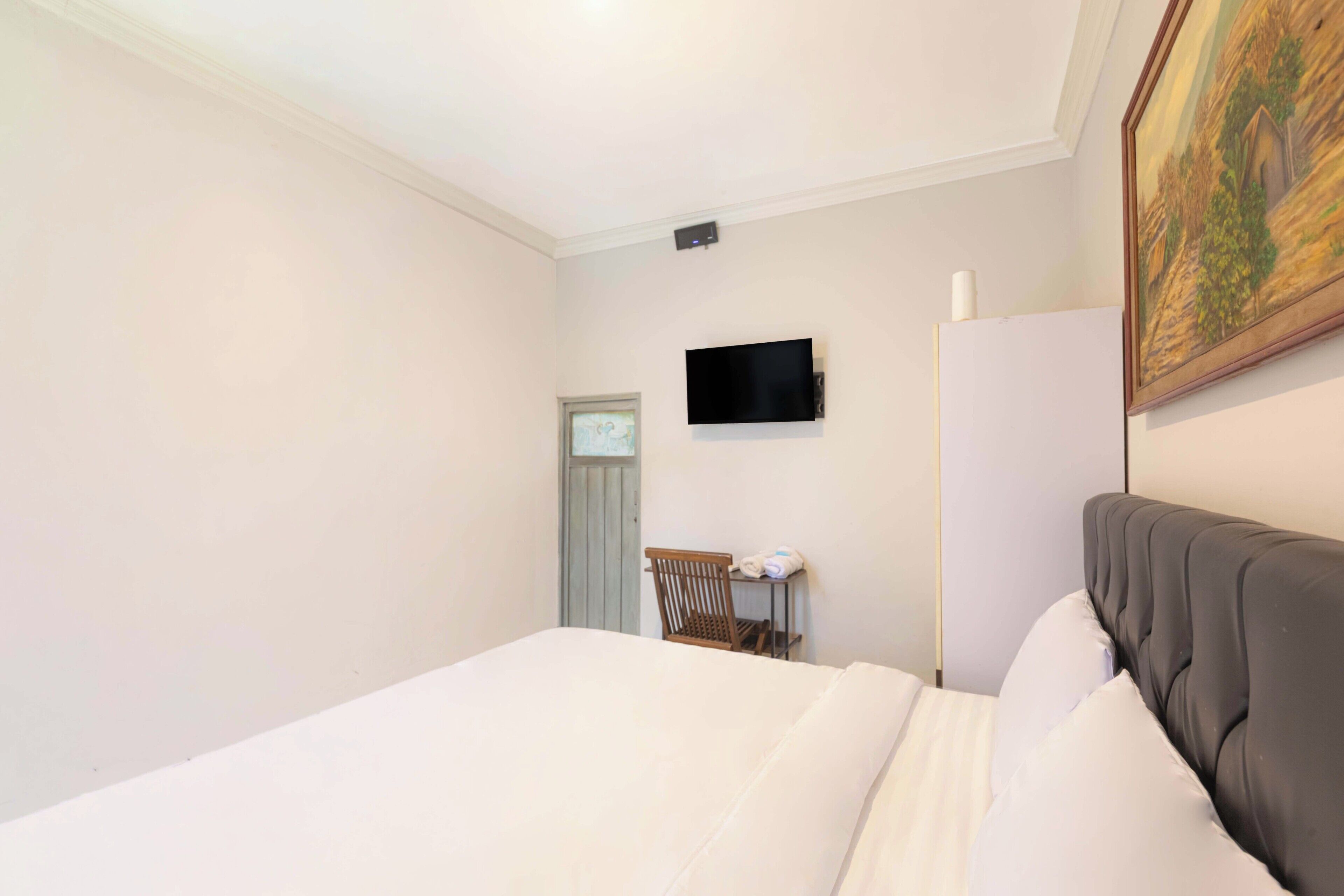 A bedroom with a bed, a television mounted on the wall, a chair, and a door.