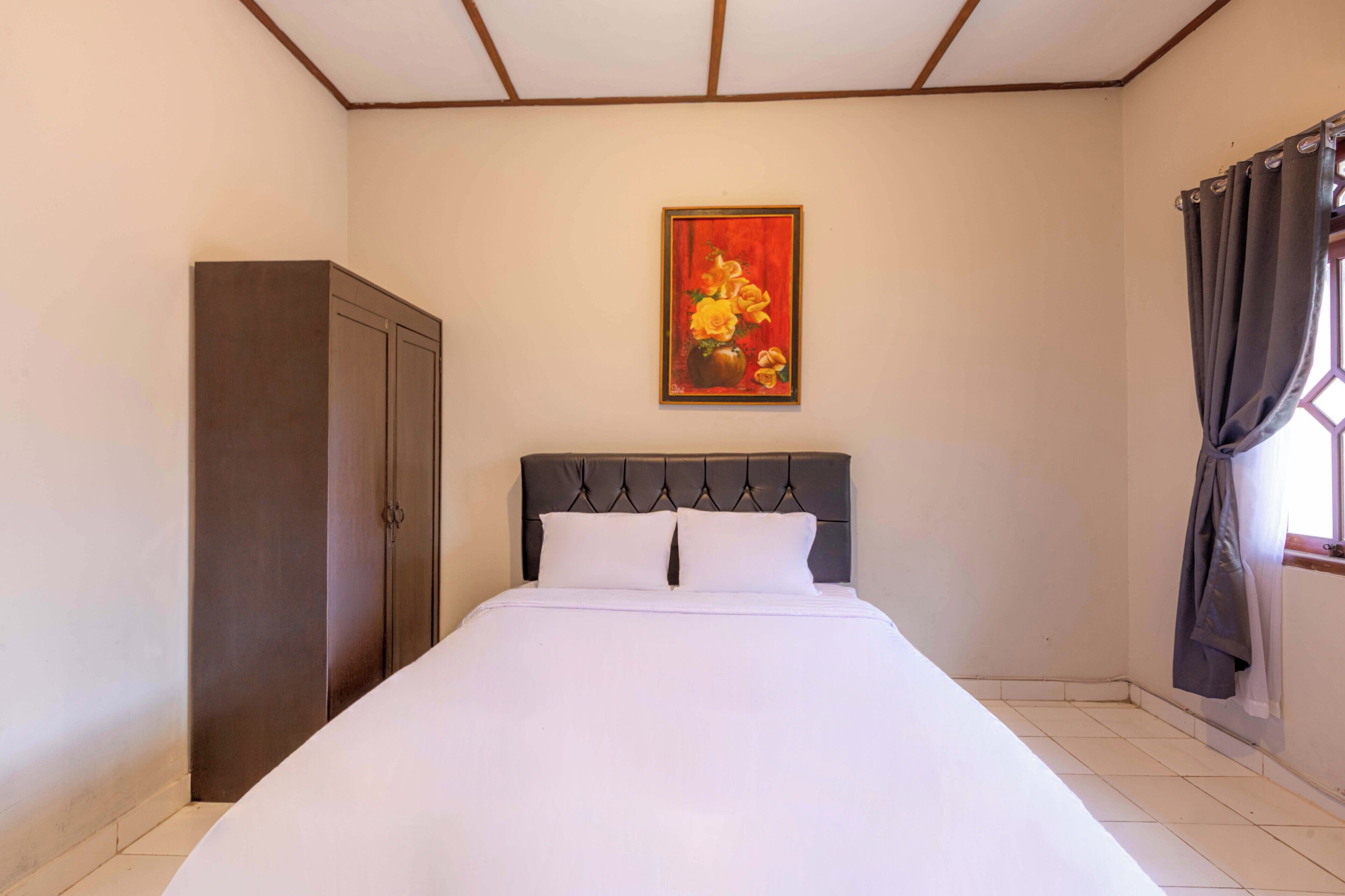 Une chambre à coucher avec un lit, une armoire, un tableau au mur et une fenêtre avec des rideaux.