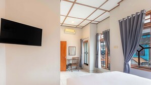 Hotellihuone, jossa on sänky, seinälle asennettu televisio, ikkuna verhoilla ja näkymä ulos.