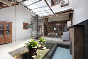 A covered patio with a pool, potted plants, a wooden cabinet, and a staircase. - Agni Homestay (Yogyakarta)
