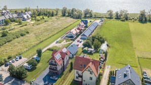 An aerial view of a residential area with houses, a long row of parked cars, and a body of water in the background. - Apartment with a balcony, garden with barbecue (Krynica Morska)