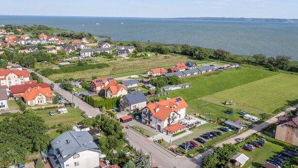 An aerial view of a coastal residential area with houses, a marina, and a large green field.