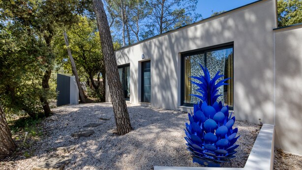 A modern building with large windows, a gravel pathway, and a blue sculpture in the foreground. - Holiday Home “Nestled Among the Pines” with Wi-Fi and Air Conditioning (Saint-Bauzille de Montmel)