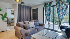 A modern living room with a sofa, a coffee table, and a large window with curtains. - Holiday Home “Nestled Among the Pines” with Wi-Fi and Air Conditioning (Saint-Bauzille de Montmel)