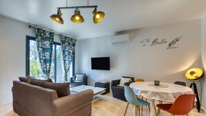 A modern living room with a sofa, dining table, chairs, and a flat-screen TV. - Holiday Home “Nestled Among the Pines” with Wi-Fi and Air Conditioning (Saint-Bauzille de Montmel)