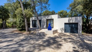 A modern building with a garage, surrounded by trees and gravel. - Holiday Home “Nestled Among the Pines” with Wi-Fi and Air Conditioning (Saint-Bauzille de Montmel)