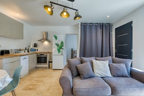 A modern kitchen with a dining area, a sofa, and a door leading to another room. - Holiday Home “Nestled Among the Pines” with Wi-Fi and Air Conditioning (Saint-Bauzille de Montmel)