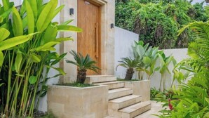 Un edificio moderno con puerta de madera, una serie de escalones de piedra que conducen a una puerta y exuberante follaje alrededor de la entrada.