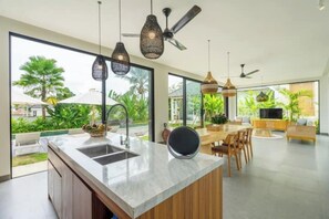 A modern kitchen with a large island, built-in cabinets, and pendant lighting. - Villa Gantari by GORO (Gianyar Regency)