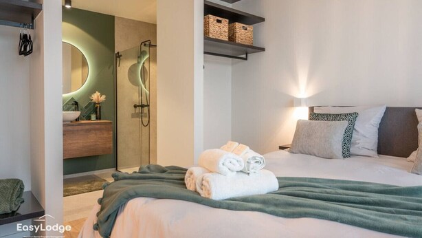Un dormitorio moderno con cama, mesita de noche, espejo, ducha y estanterías empotradas.
