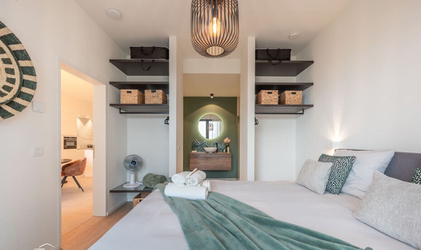 A modern bedroom with a bed, a bedside table, a mirror, and built-in shelving with baskets.