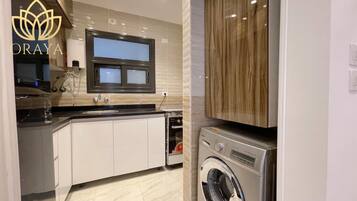 A modern kitchen with a built-in washer and dryer, a window above the sink, and a countertop with a glass of water.
